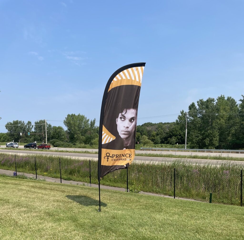 A sign on the grass with image of Prince on it.